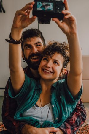 Joyful couple embracing and taking selfie on camera at home