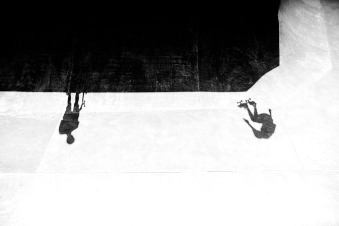 Grayscale photo of shadow of two people playing skateboards