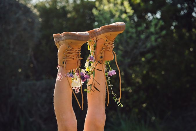 Crop person wearing boots with flowers lying in nature