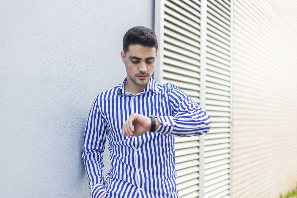Young man standing outdoors and checking his wrist watch