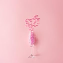 Champagne glass with pink glitter on pastel pink background
