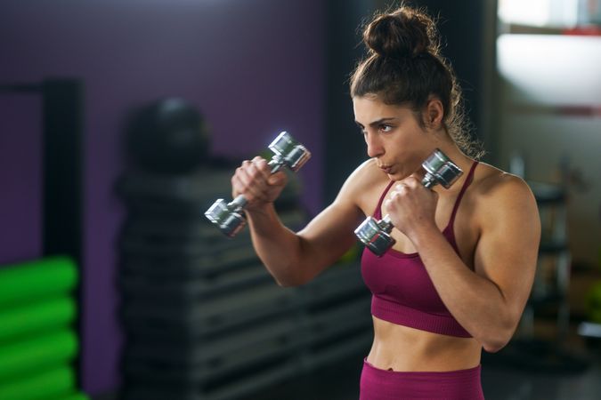Muscular woman in gym holding small dumbbells up