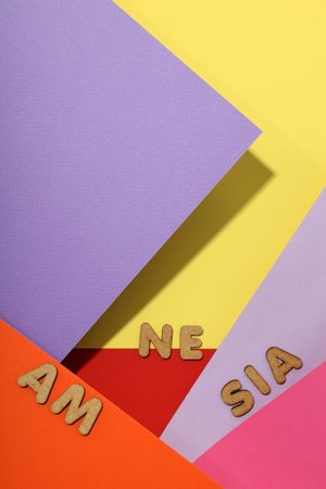 Scattered brown letters spelling “amnesia” on colorful paper background, vertical