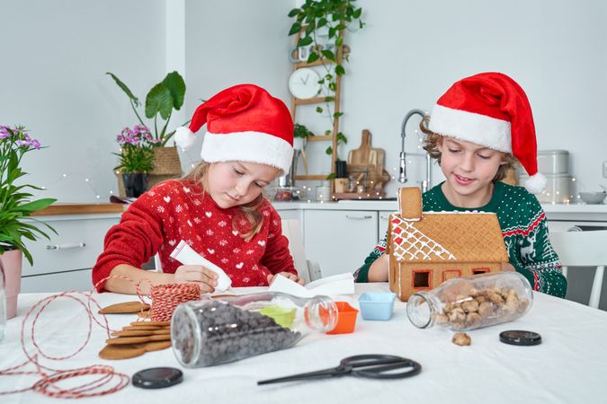 Cute children making gingerbread house in kitchen