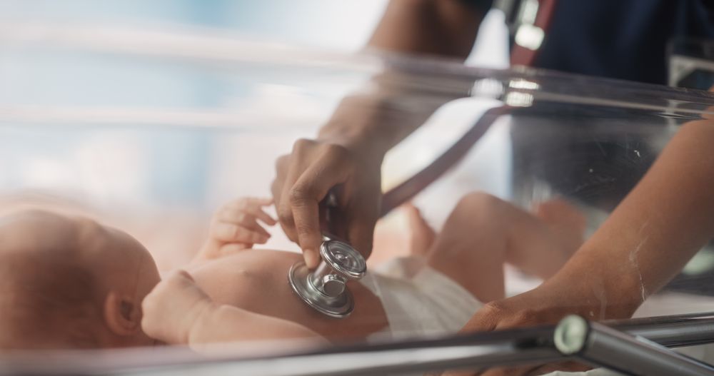 Black Female Pediatrician Uses Stethoscope to Listen to Heartbeat and Lungs of Recovering Newborn Baby Resting in Bassinet.