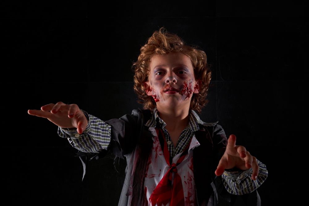 Child disguised as zombie with blood and glitter with arms raised walking