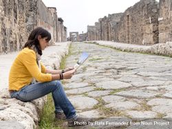 Side view of a woman in yellow checking tourist map of ancient ruins 5qkyda