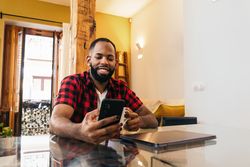 Black man using smartphone while having coffee at home