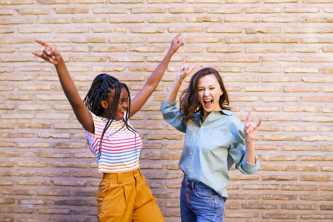 Two female friends with their arms up in celebration against a brick wall