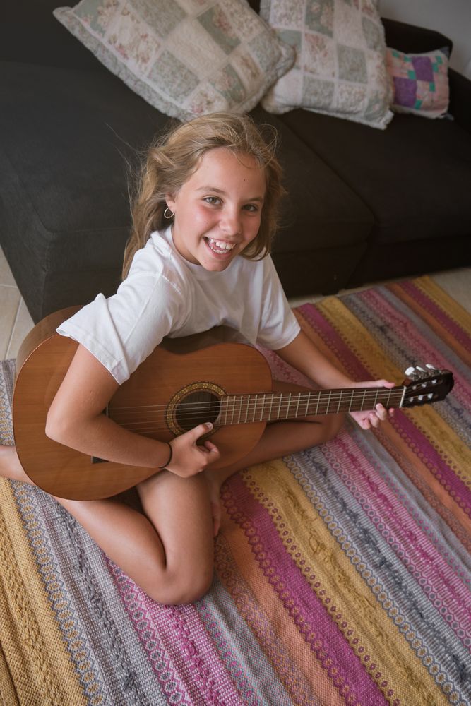 Positive kid sitting on floor and playing guitar