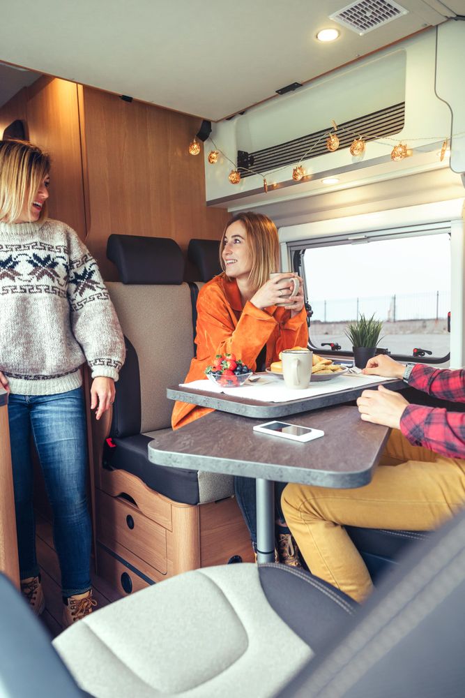 Women in warm sweaters having breakfast in back of van, vertical