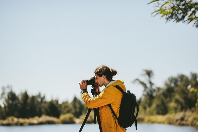 Man standing beside a lake taking photos of nature on a sunny day