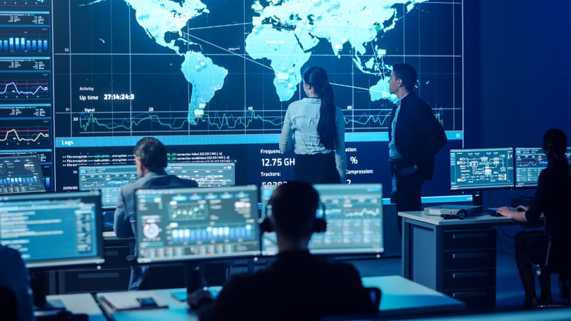 In a High-tech Control Room, Diverse Professionals Analyze Global Data on Large Screens, Enhancing Cybersecurity Strategies and Decision-making Through Collaborative Efforts and Real-time Insights.