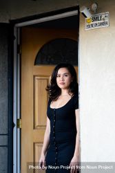 Woman looking seriously at camera leaning against her doorway at home 49mDW4