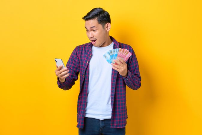 Surprised man with cash in one hand and a smart phone in the other