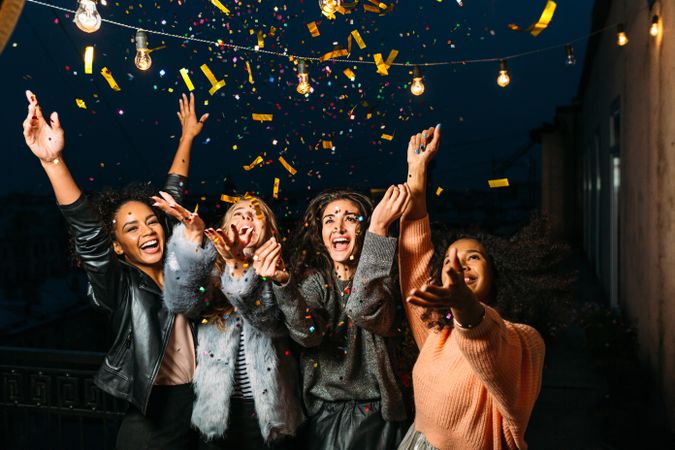 Group of multi-ethnic female friends throwing confetti at night