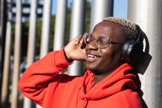 Cheerful Black male listening to music in headphones while chilling in park