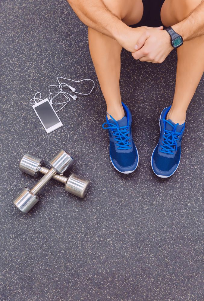 Top view of person sitting next to phone and silver weights in gym