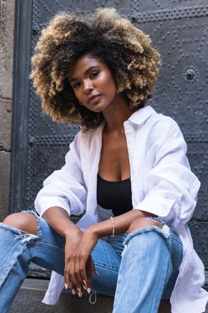 Stylish Black woman sitting on concrete steps near gates