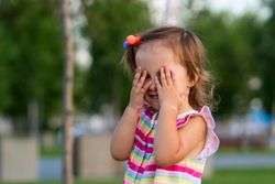 Toddler covering eyes in park outdoors