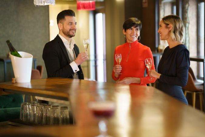 Three well dressed people standing with Prosecco or cava in bar