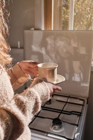Unrecognizable woman with cup of coffee in kitchen