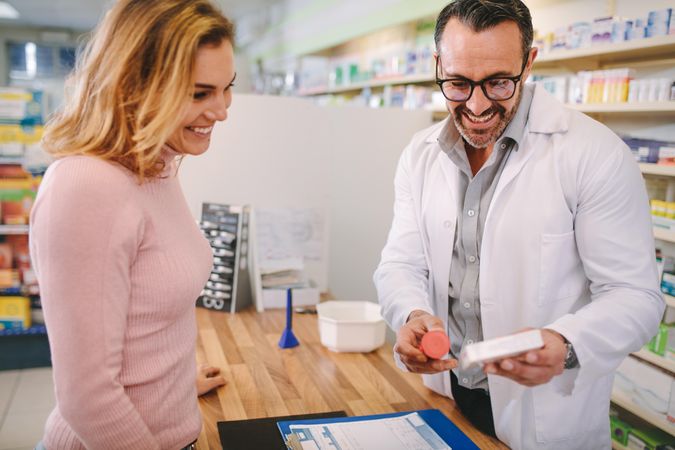 Pharmacist showing and advising medicine to female customer in chemist shop