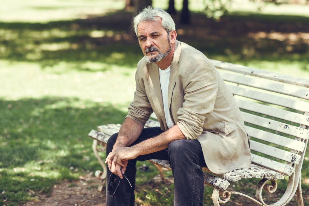 Portrait of a mature man, sitting forward on bench in a park