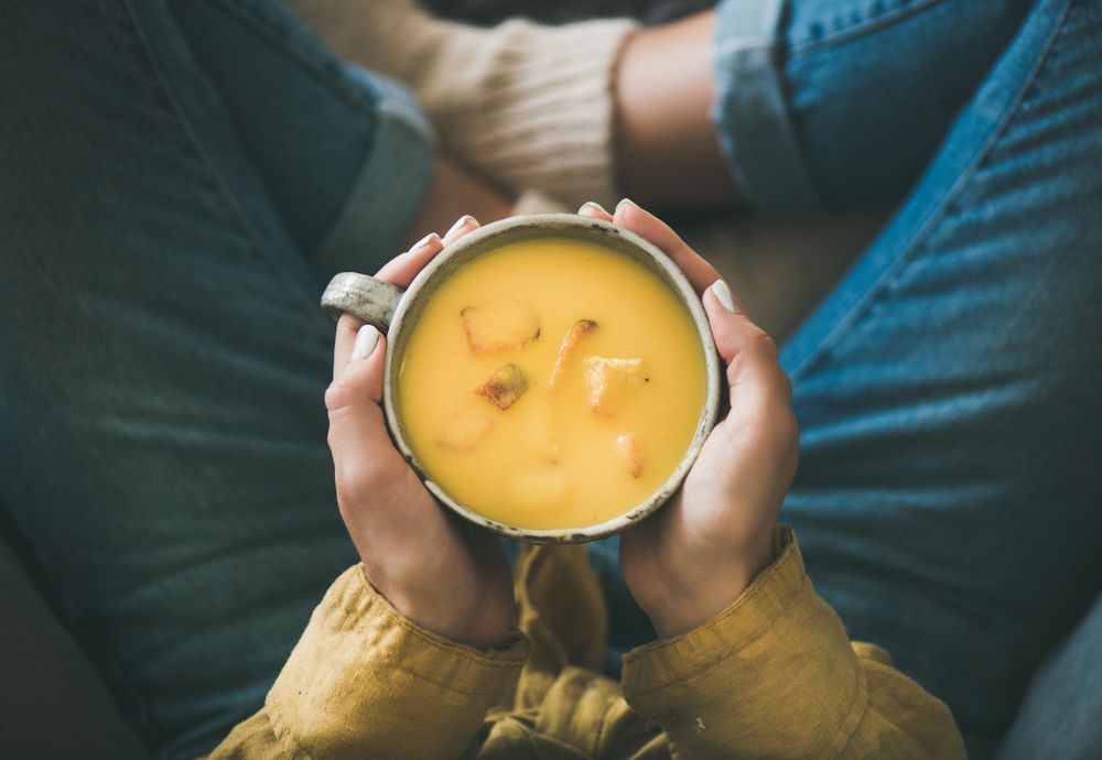 Woman in jeans holding cup of squash soup