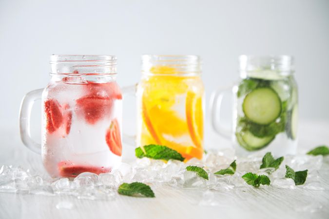 Three mason jars of infused water surrounded with ice and mint leaves