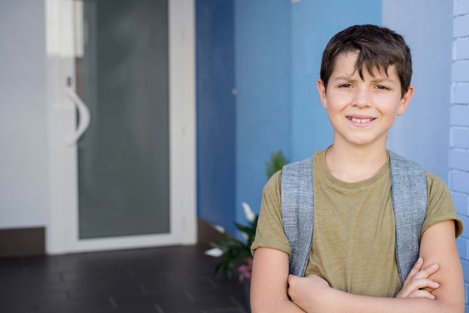 Portrait of boy in backpack standing in school with arms crossed