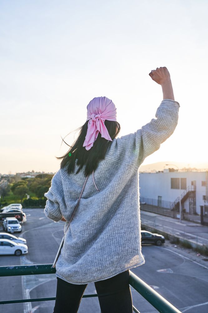 Woman in pink scarf raising fist against breast cancer