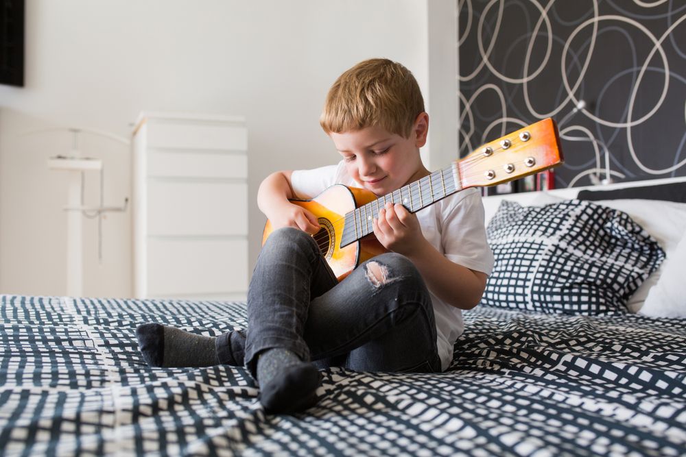 Young blonde boy playing toy guitar