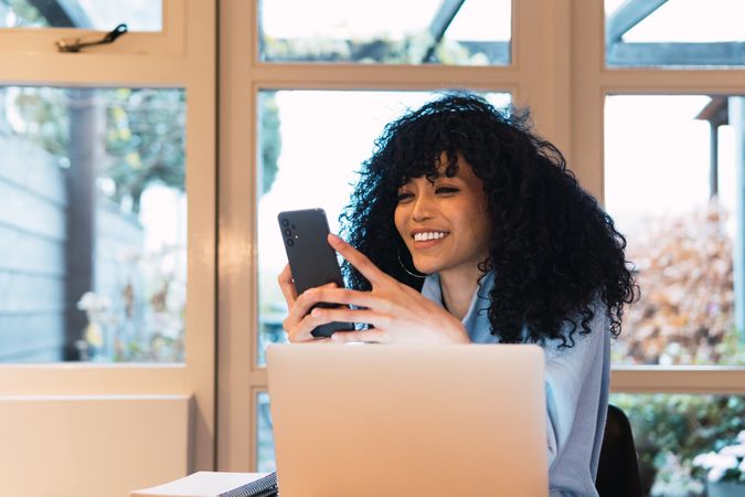 Cheerful Black woman using smartphone and laptop