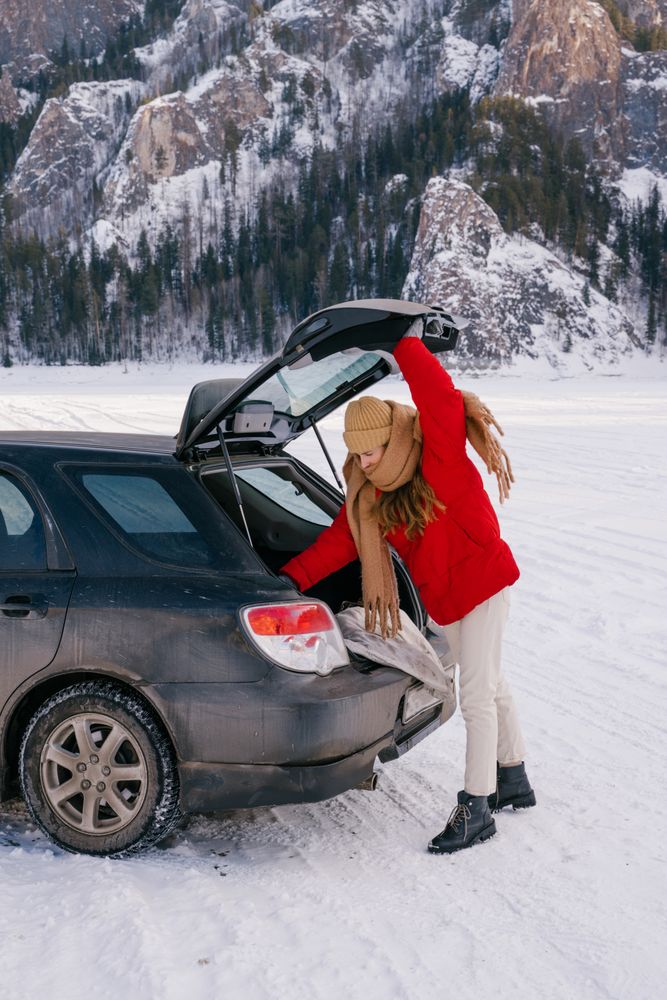 Female traveler standing in snowy valley and opening car trunk