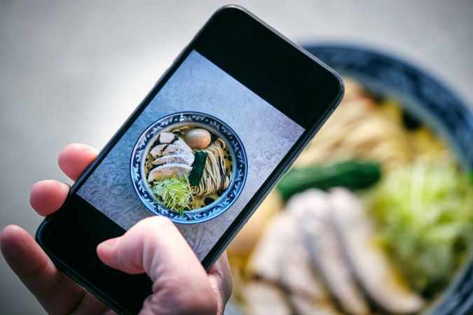 Crop blogger taking photo of ramen on smartphone