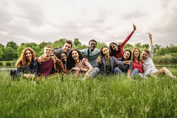 Multi-ethnic group of friends cheering looking at the camera sitting in the meadow