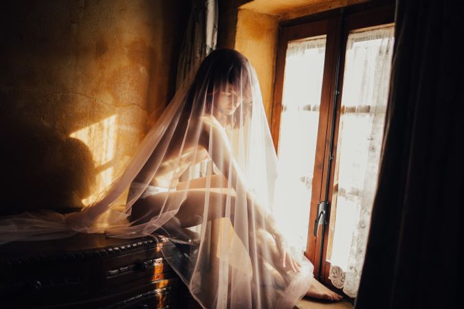 Sensual woman under veil near window