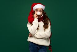 Girl in Santa hat playfully holding pompom near face.