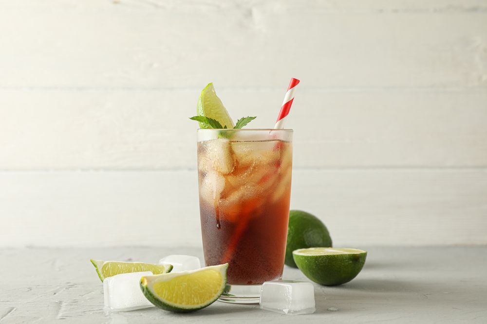Glass with cold cola and citrus on grey cement background, space for text