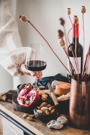 Rustic setting of women holding wine, with cheese, long candles, pomegranate, and dried poppies