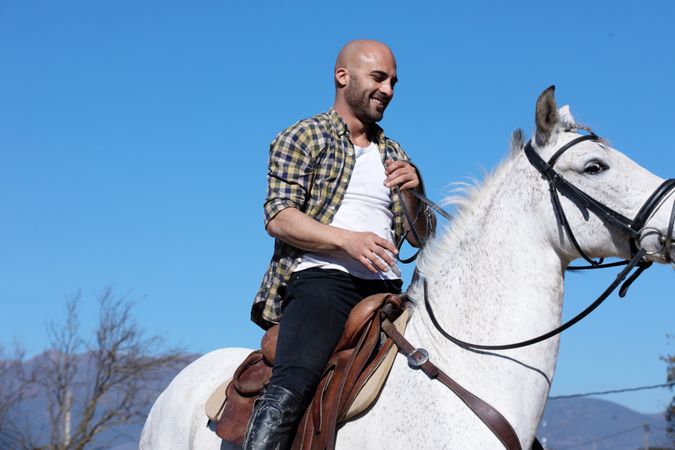 Smiling man in checkered shirt riding horse