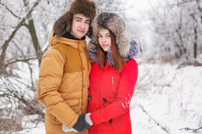 Teenage boy and girl standing in snowy forest in winter coats and fur hat