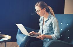 Serious female businesswoman working on laptop on sofa