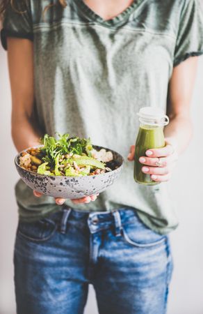 Woman in green t-shirt standing holding vegetarian bowl and green smoothie