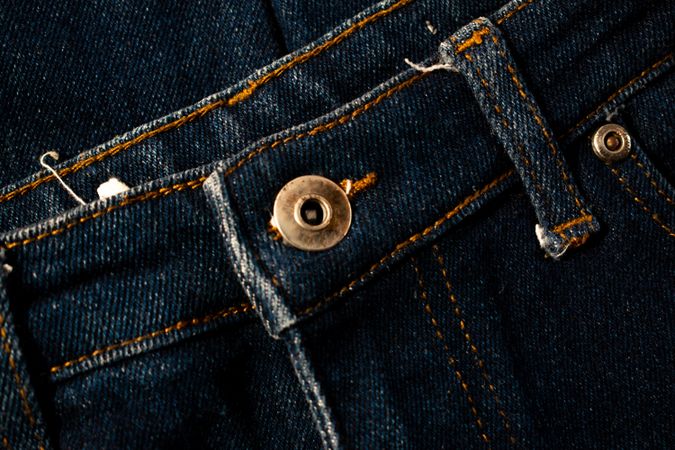 Close up gold and shiny button navy blue jeans fabric background texture.
