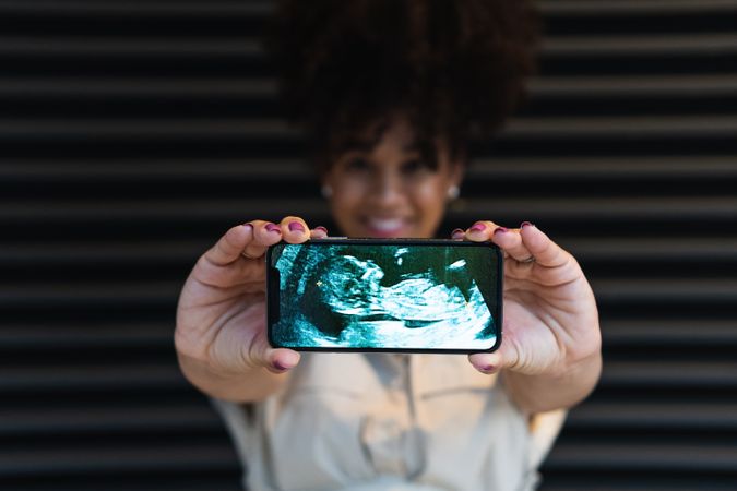 Smiling Black woman showing smartphone screen with baby ultrasound
