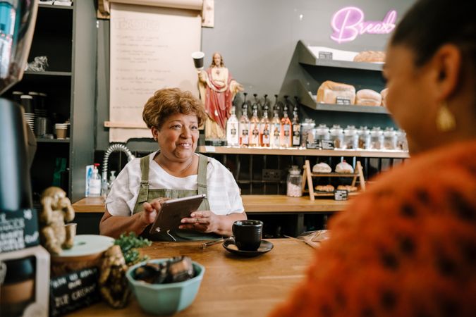Older Black woman ringing up order on digital tablet in coffee shop