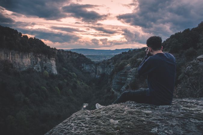 man with photo camera sitting on hill mountain with magnificent sunset