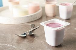 Composition with plastic cups with yogurt on grey table, space for text